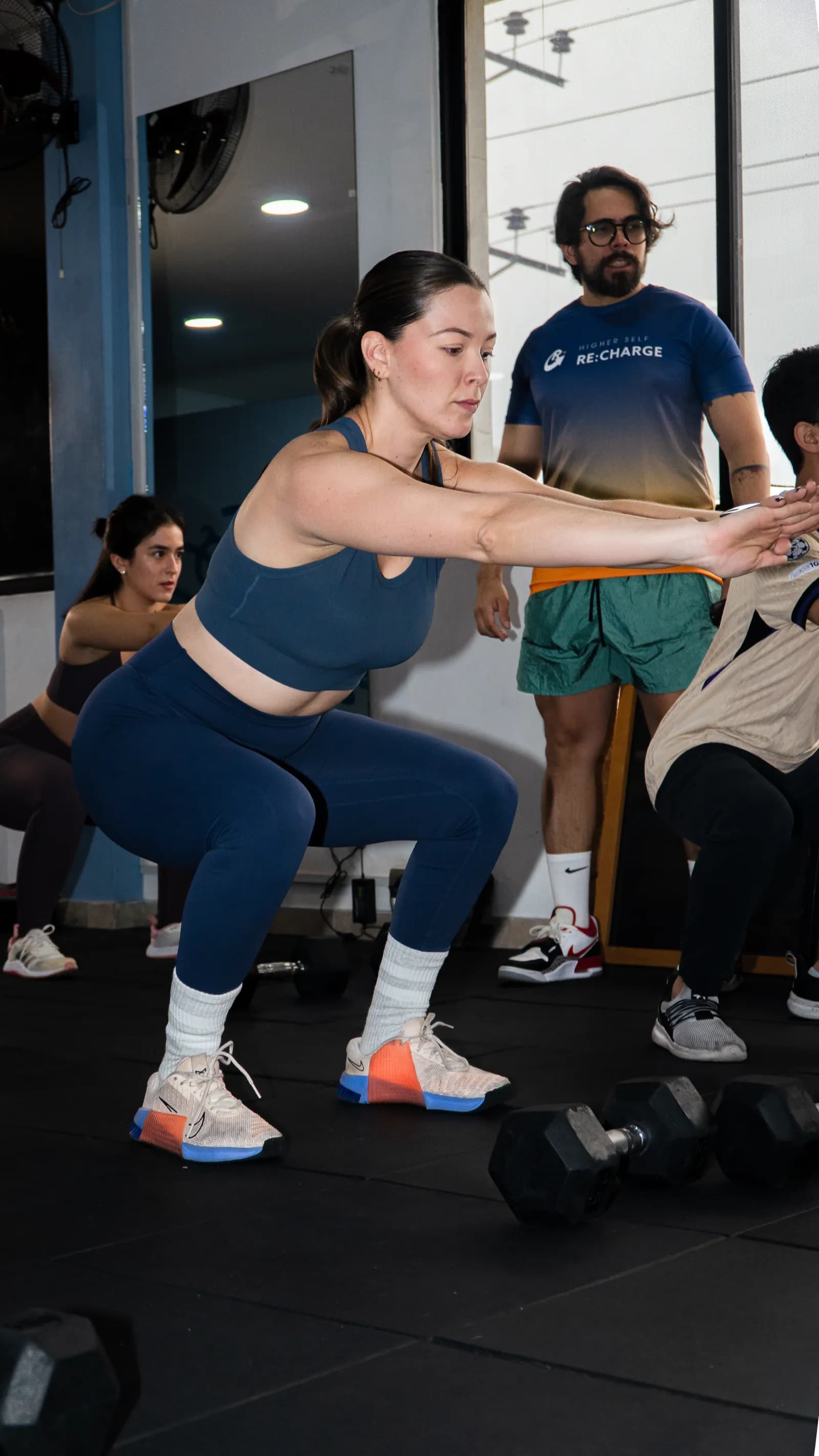Atleta haciendo sentadilla junto a su coach en el piso de entrenamiento de ReCharge
